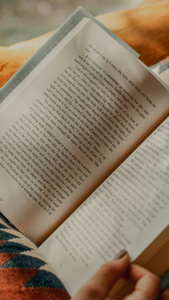 person reading book on brown and beige textile